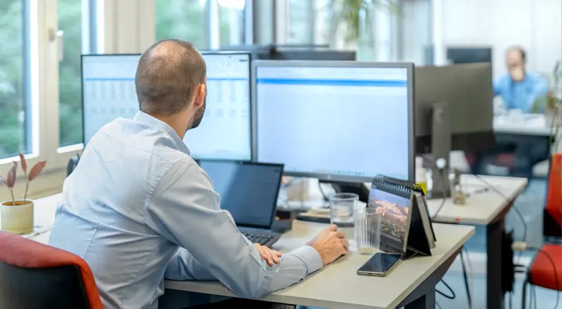 Ein Mitarbeiter von Datalizard sitzt am Bürotisch und schaut auf 2 grosse Bildschirme.